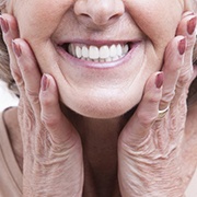 older woman holding face with dentures in Pepper Pike