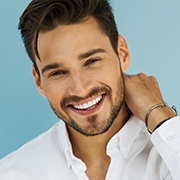 A young man wearing a white button-down shirt and smiling after learning about the cost of porcelain veneers in Pepper Pike