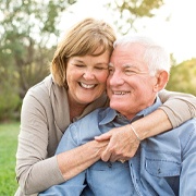 Older woman hugging her husband while outside after all on four dental implants