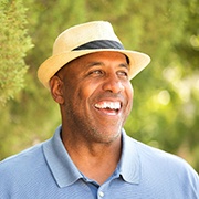 older man with dentures wearing a blue polo smiling in front of trees