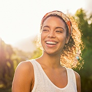 Woman in white tank top smiling after emergency dentistry