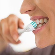Closeup of woman brushing her teeth with an electric toothbrush to prevent dental emergencies
