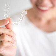 Woman in white shirt holding Invisalign clear aligner