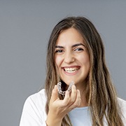 Woman smiling while holding Invisalign tray