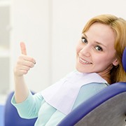 Woman smiling in dental chair with thumbs up after porcelain veneers