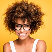 A young female wearing a white tank top and black glasses shows off her new and improved smile with porcelain veneers