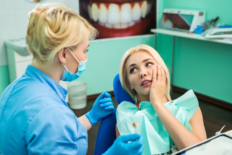 a young female holding her cheek in pain while listening to her dentist