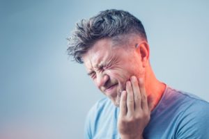 man with a toothache holding his cheek in pain 